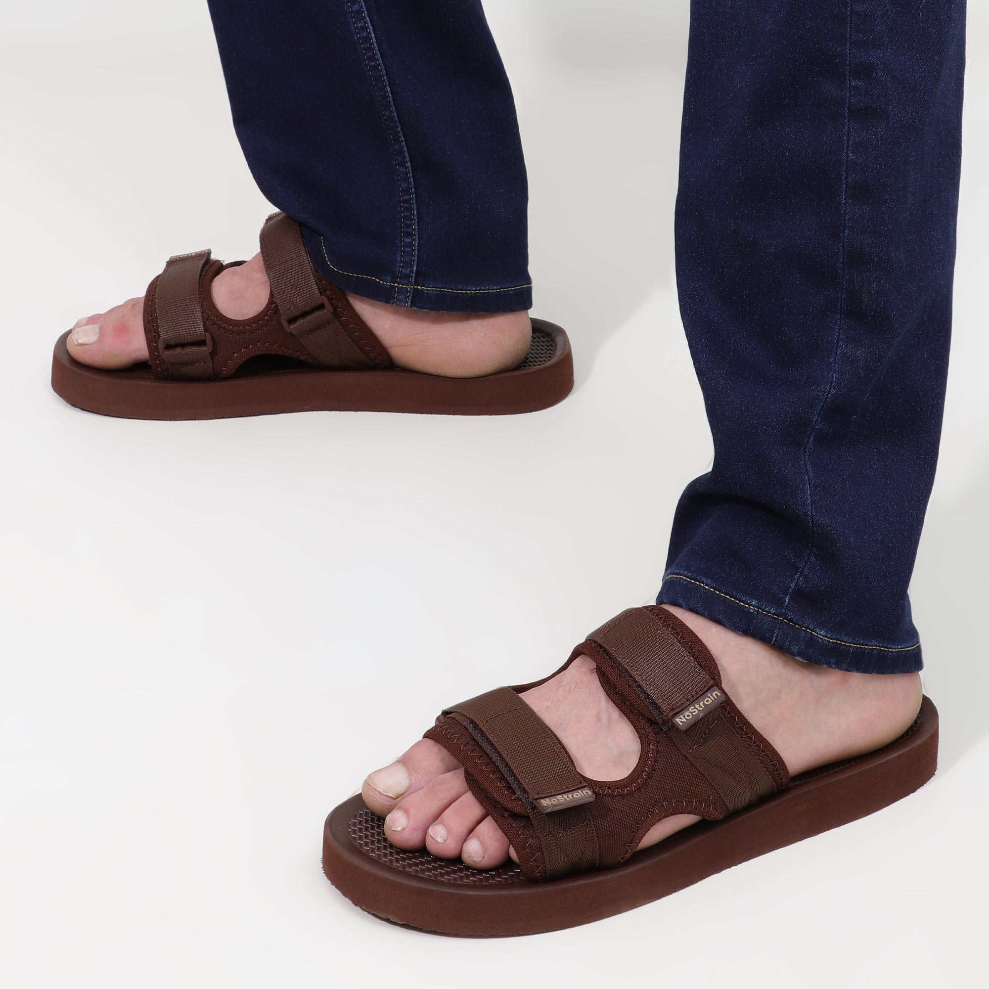 Brown sandals worn with blue jeans on a white background