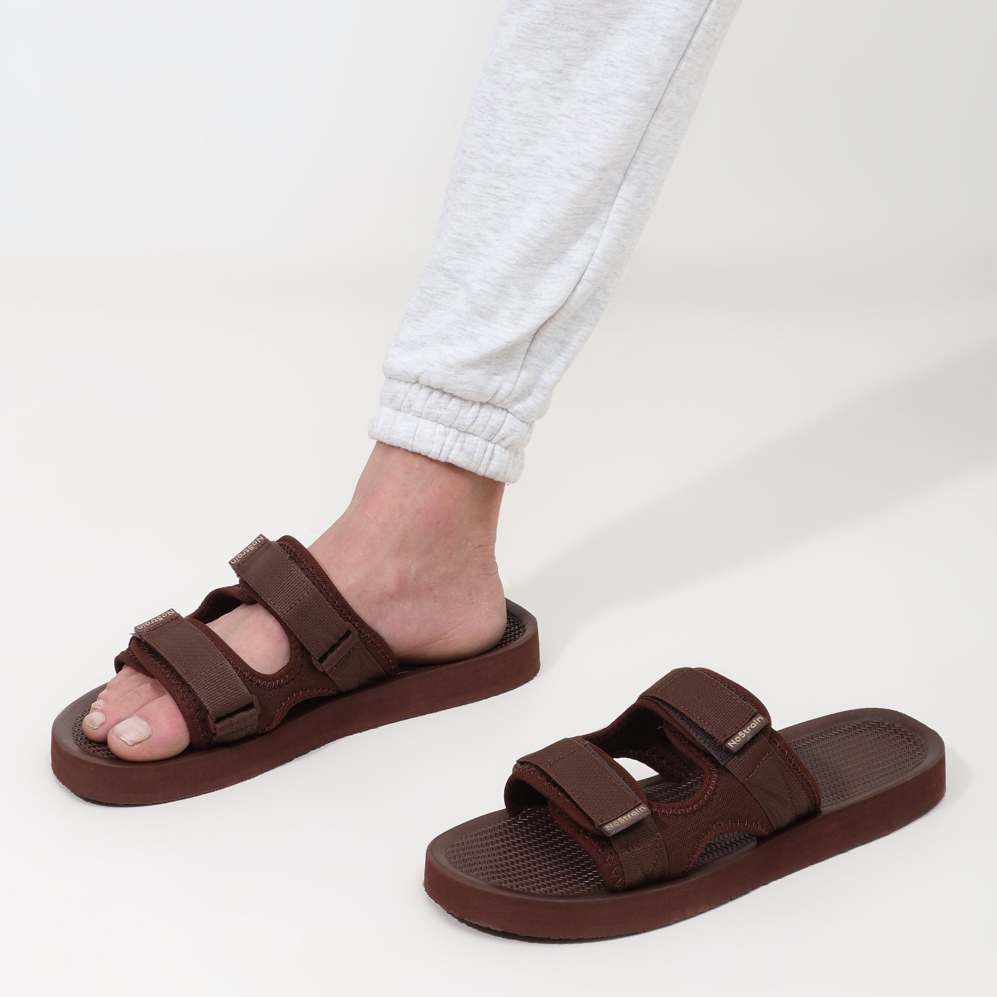 Brown sandals worn with light-colored pants on a white background