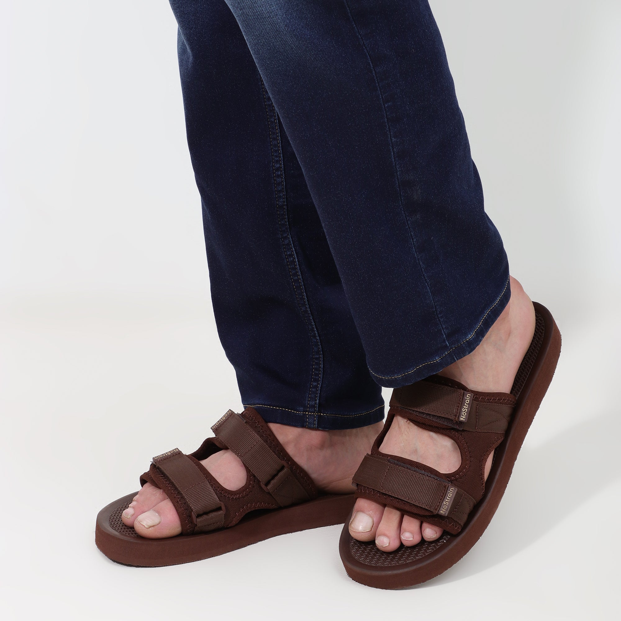 Brown sandals worn with dark blue jeans on a light gray background